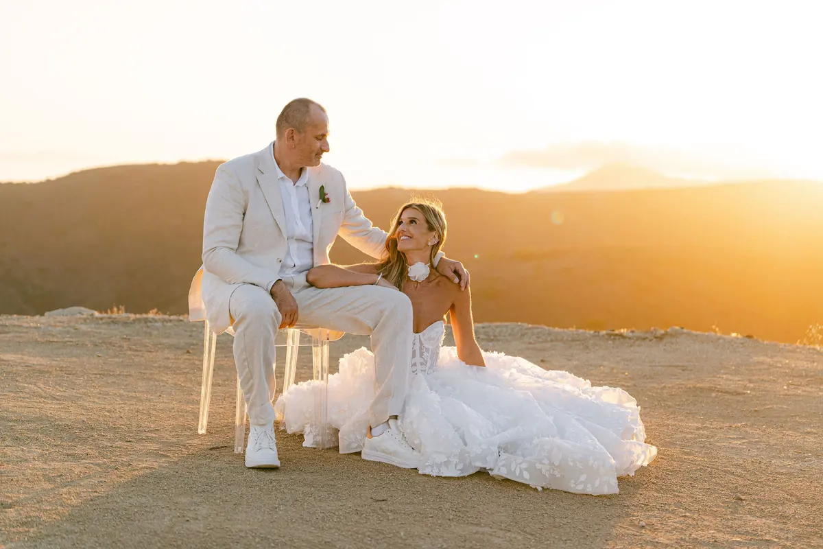 A bride and groom share a quiet, romantic moment at sunset, surrounded by golden light and rolling hills.