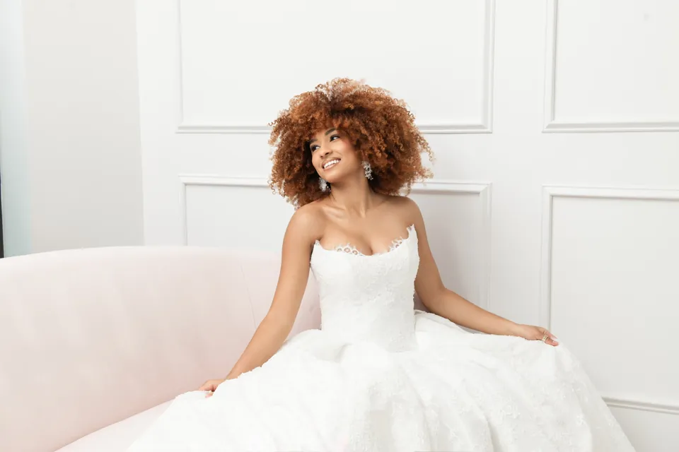 A smiling bride in a lace ballgown on a blush sofa in a Savvy Bridal suite