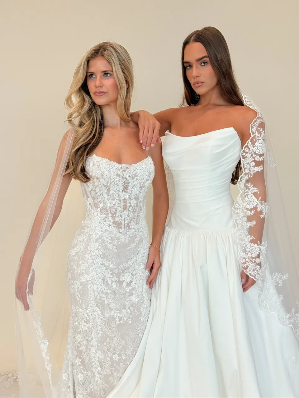 Two brides in gowns from the Savvy collection: a beaded lace fit-and-flare and a draped satin ballgown