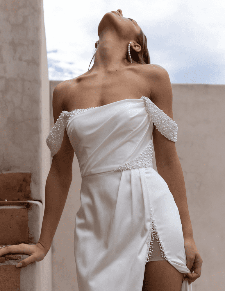 A close up of a short, white wedding gown with sheer off-the-shoulder sleeves.