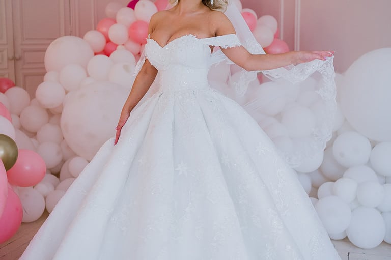 woman with large bust wearing wedding dress, with white and pink balloons behind her