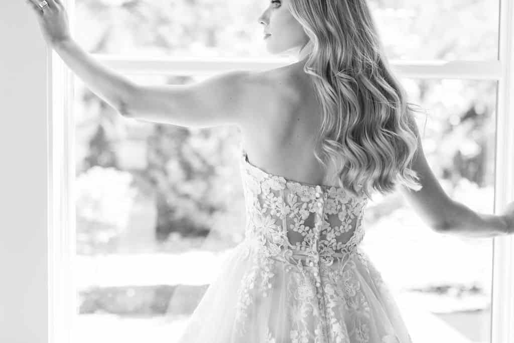 black and white image of woman in strapless wedding dress facing away from the camera and toward a window