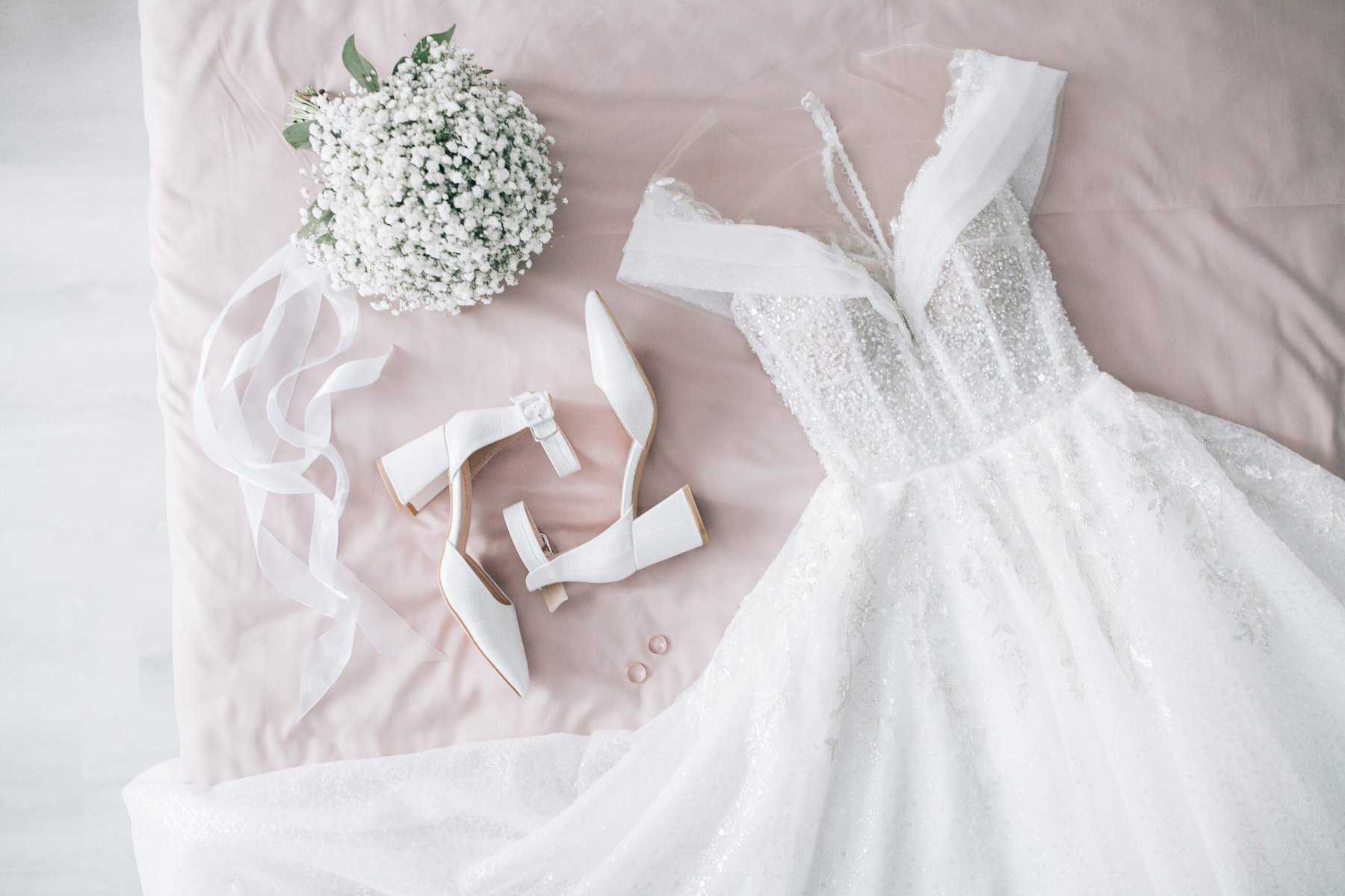 preowned wedding dress next to wedding shoes and bouquet