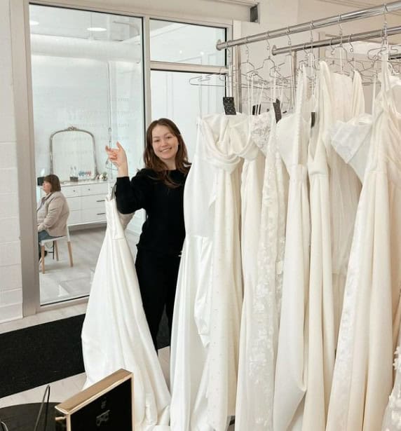 bridal stylist smiling and holding wedding dress