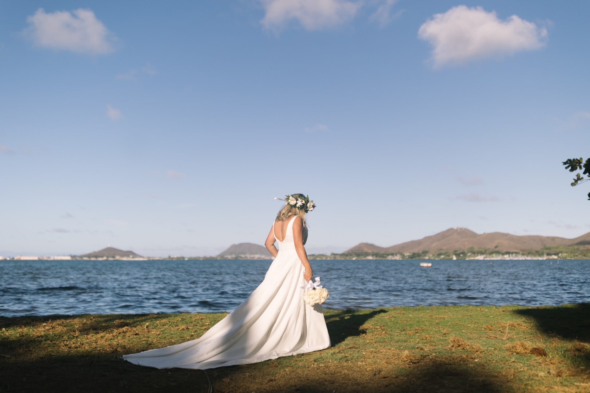 The bride wearing a a romantic V-neck gown with a flowing A-line skirt, delicate texture, and airy construction paired with white bouquet and lei to complete her look.
