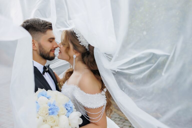Bride and groom embracing under long, white veil