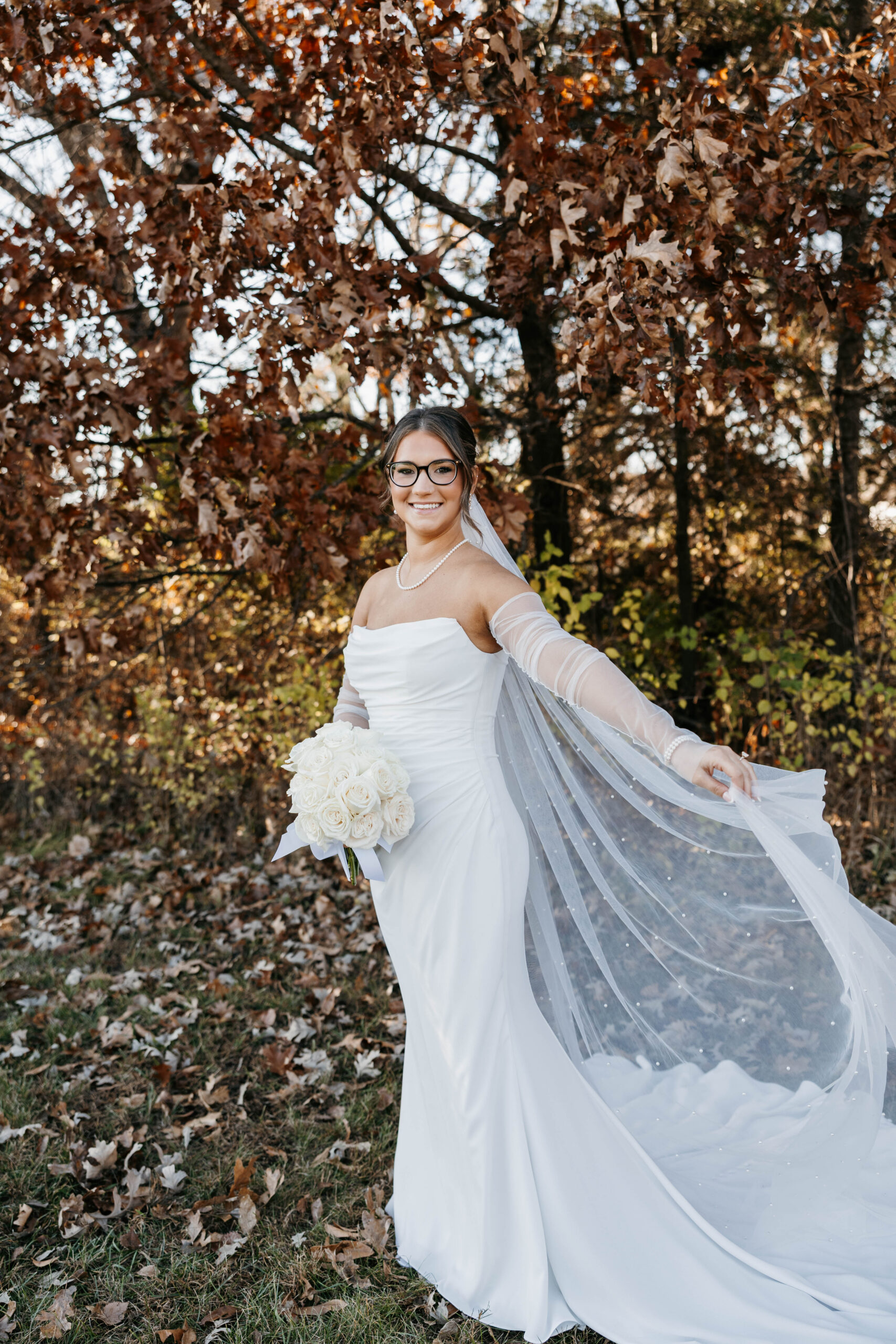 Savvy bride Dalby wearing a sleek trapless bridal gown paired with delicate sheer off-the-shoulder sleeves and a pearl-dusted veil.