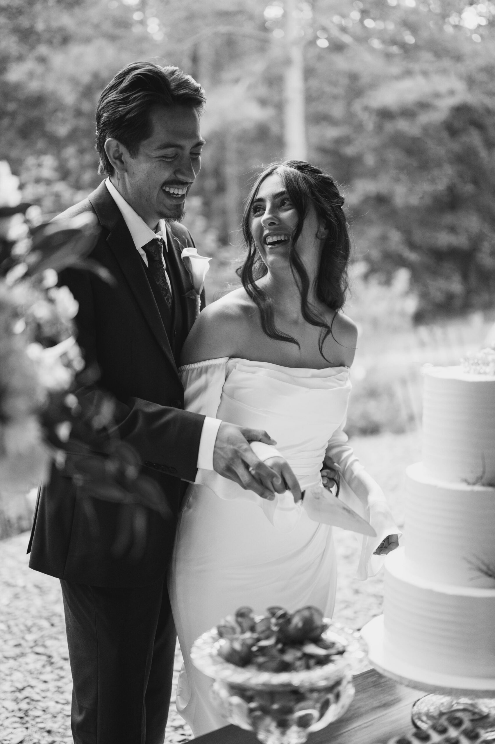happy couple smiling each other while Cake-cutting in a black-and-white photo 