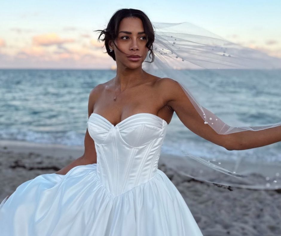 Bride wearing a strapless satin wedding dress with a pearl-embellished veil on Fort Lauderdale Beach at sunset.