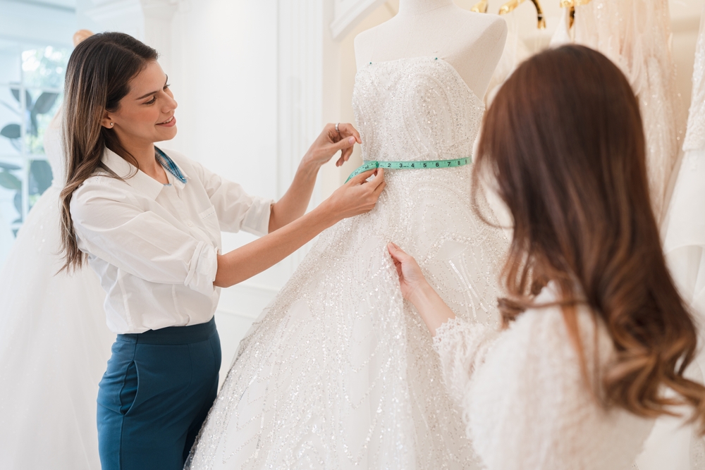 Caucasian female fashion designer being helped her customer choose wedding dress in the wedding store. wedding dress size comparison