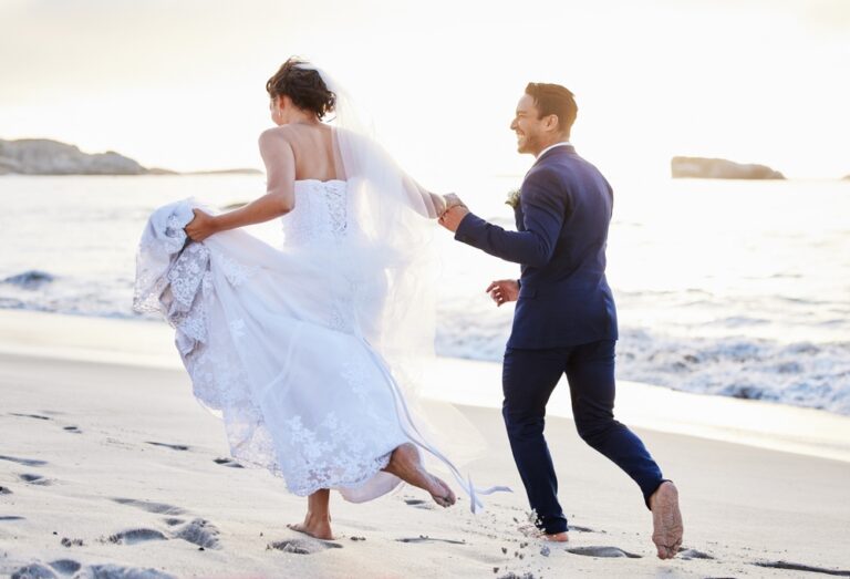 Bride and gromm running on a beach in their wedding clothes, laughing