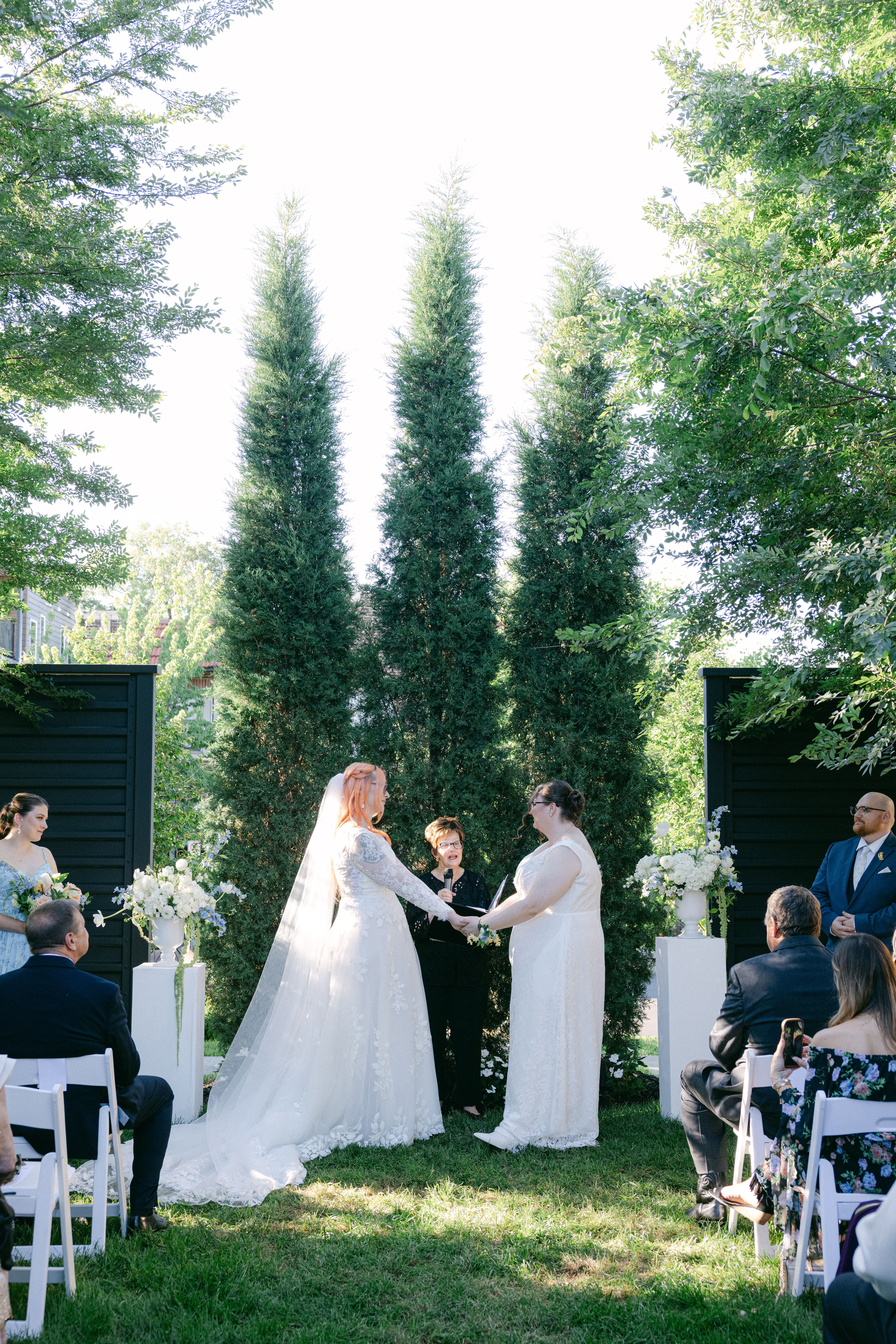 Caitlyn and Anna holding hands during their intimate outdoor wedding ceremony surrounded by family and friends.