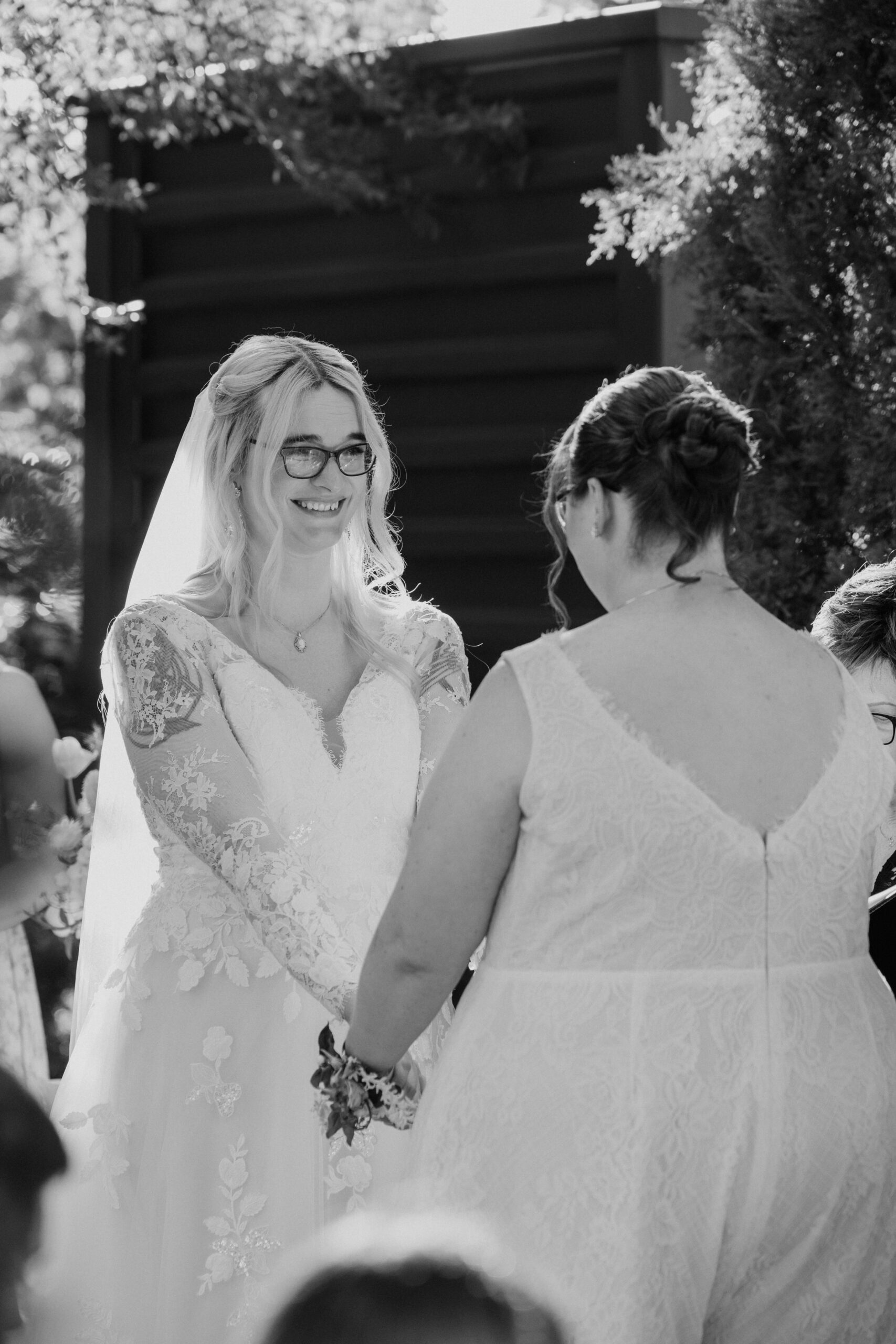 Black-and-white photo of Caitlyn and Anna smiling and holding hands during their outdoor wedding ceremony.