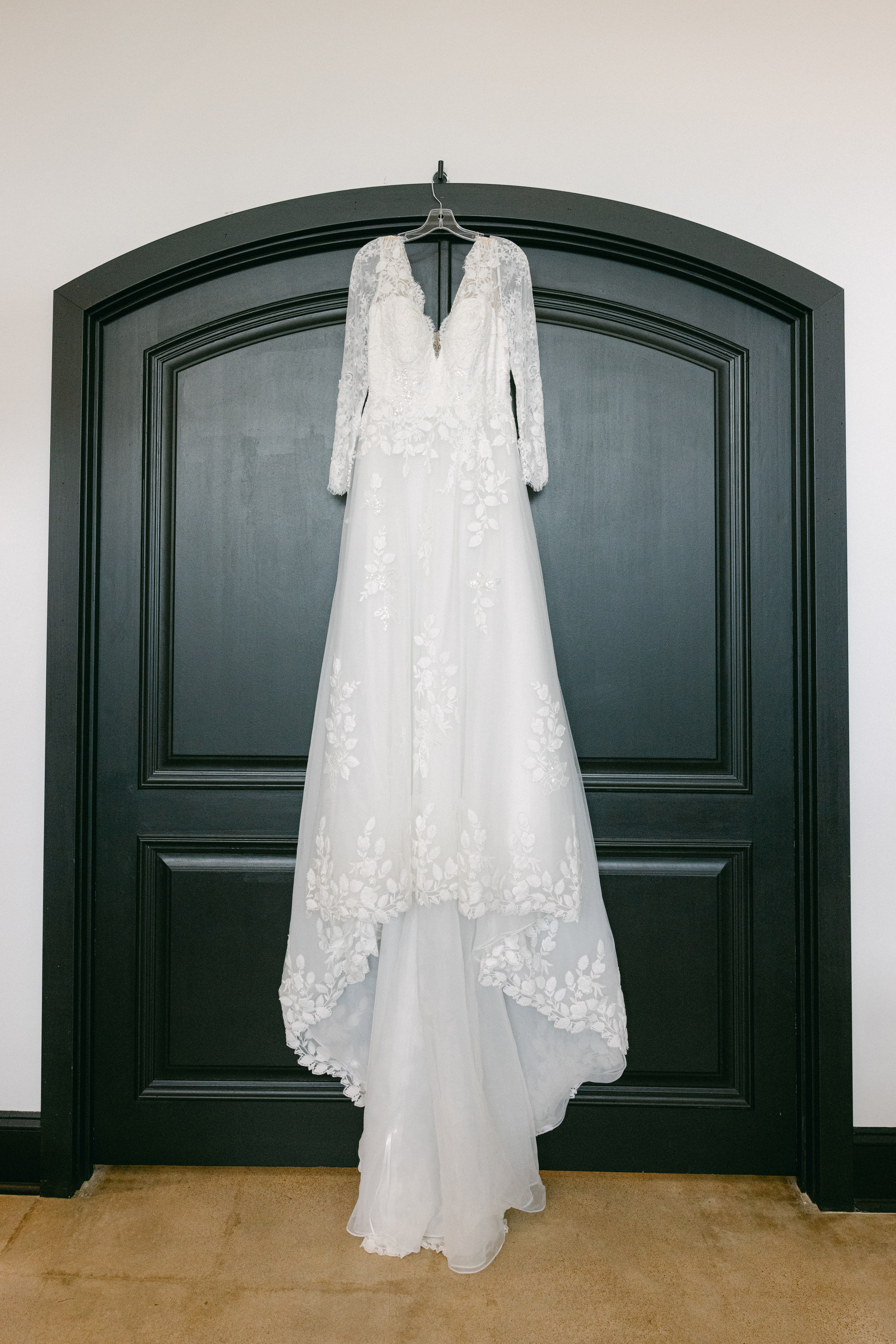 Caitlyn’s long-sleeve lace wedding dress hanging on a dark arched door before her wedding ceremony.