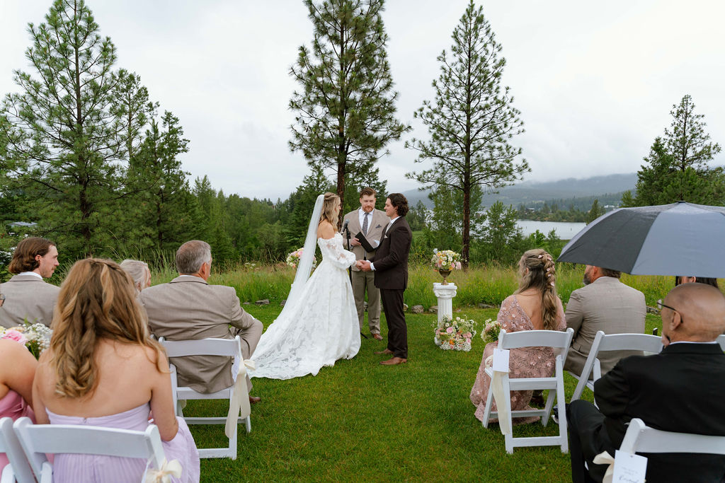 Outdoor wedding ceremony of Savvy bride Katrina and Ryon with a lake and mountain landscape behind them at Somers Mansion in Somers, Montana