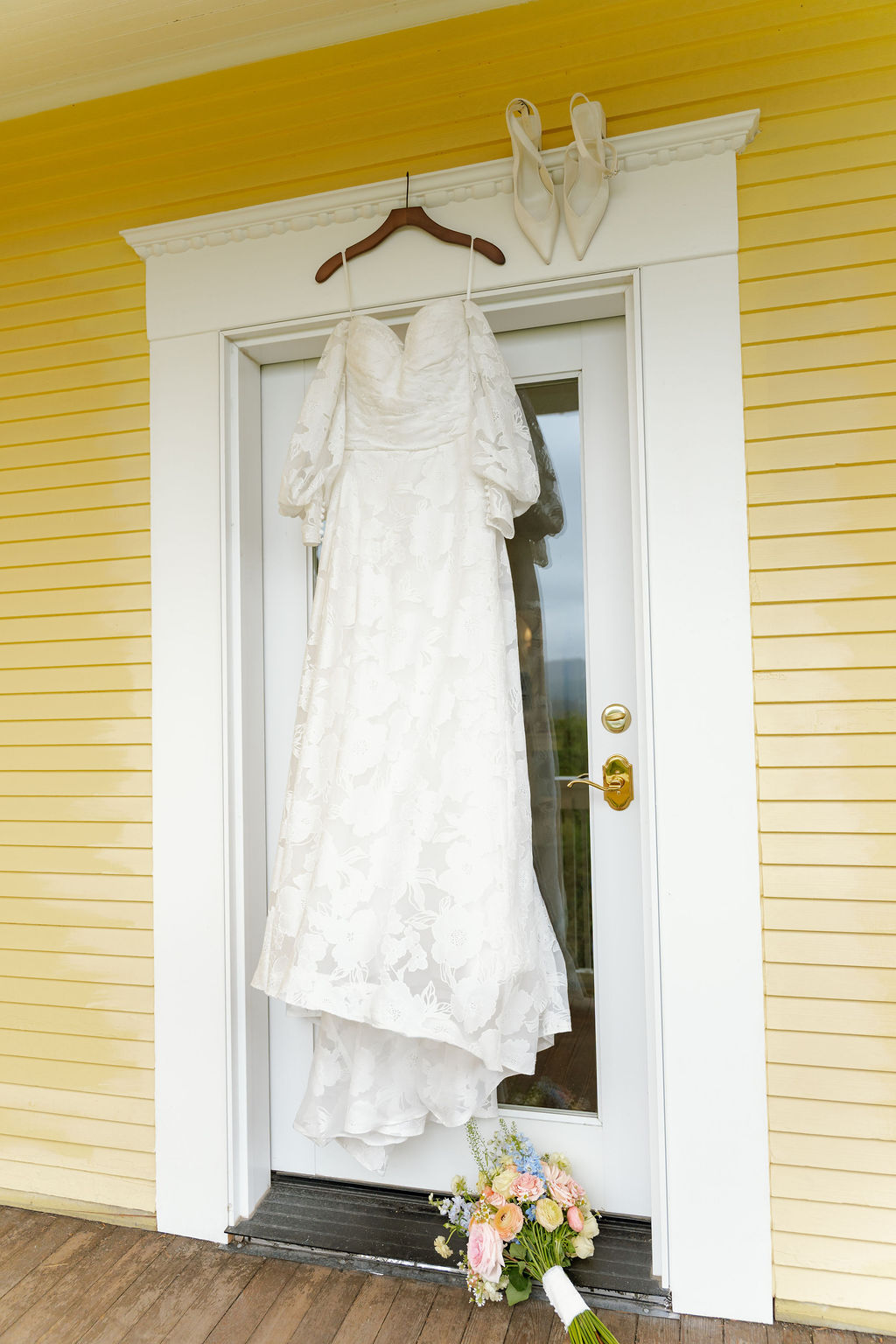 Lace wedding dress hanging beside a colorful bridal bouquet.