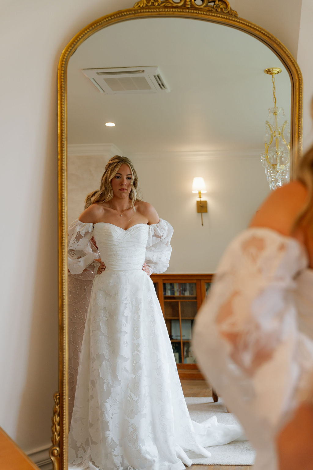 Bride admiring her lace wedding dress in a full-length mirror.