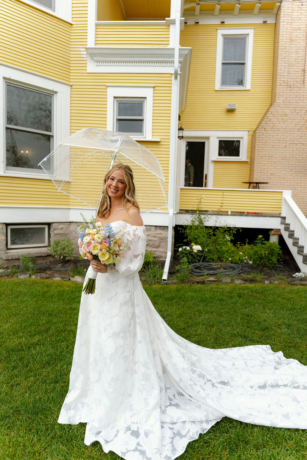 Bride holding a colorful bouquet in a lace wedding dress with a long train.