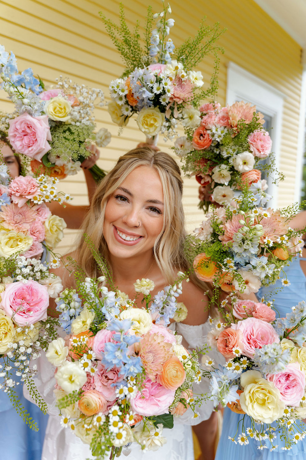 Bride Katrina smiling among colorful pink, peach, yellow and blue wedding bouquets.