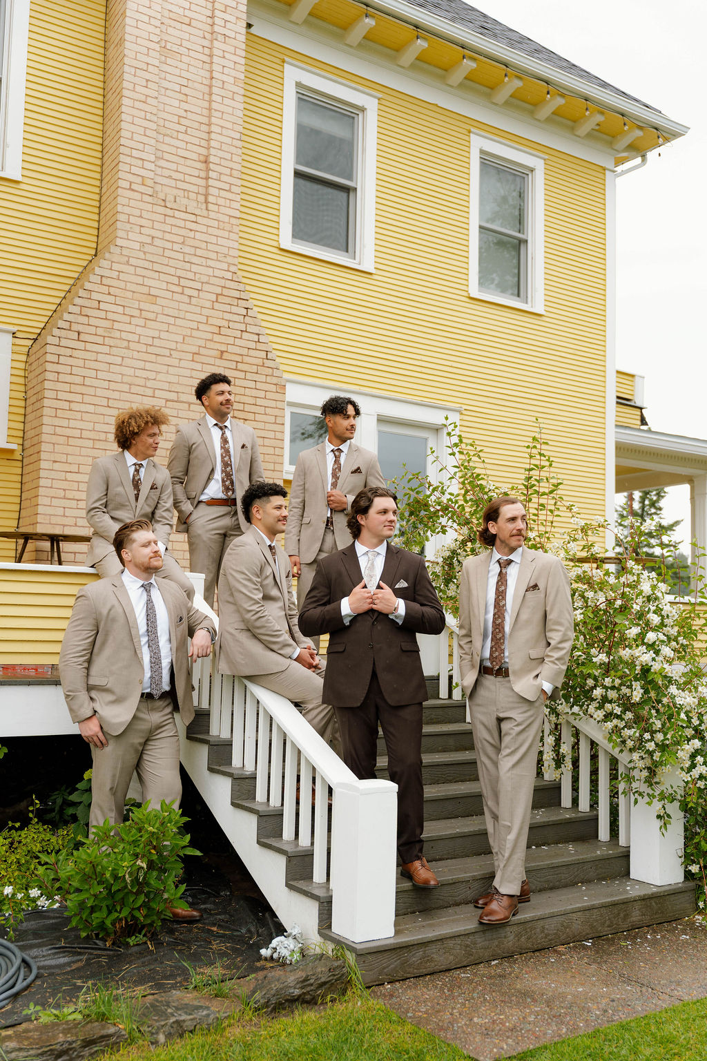 Groom and groomsmen posing together outside a yellow wedding venue.