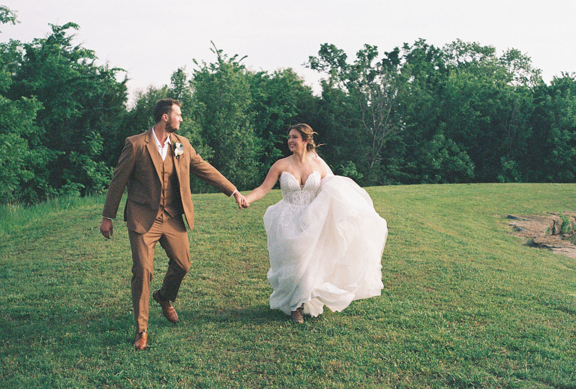 Bride and groom holding hands while walking across a grassy field on their wedding day.