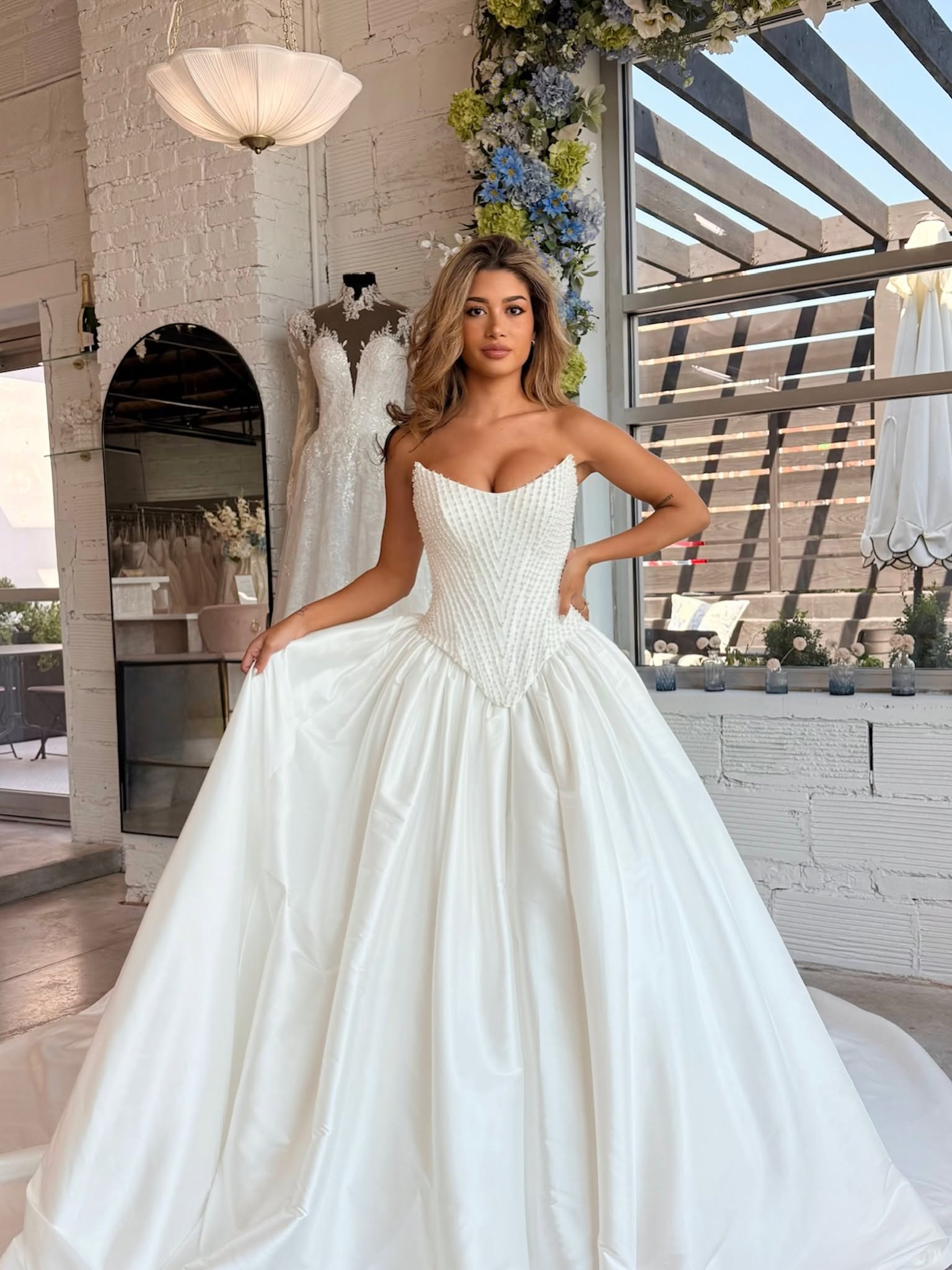 Model wearing a strapless satin ball gown with a structured basque waist corset and a voluminous skirt at Savvy Bridal.