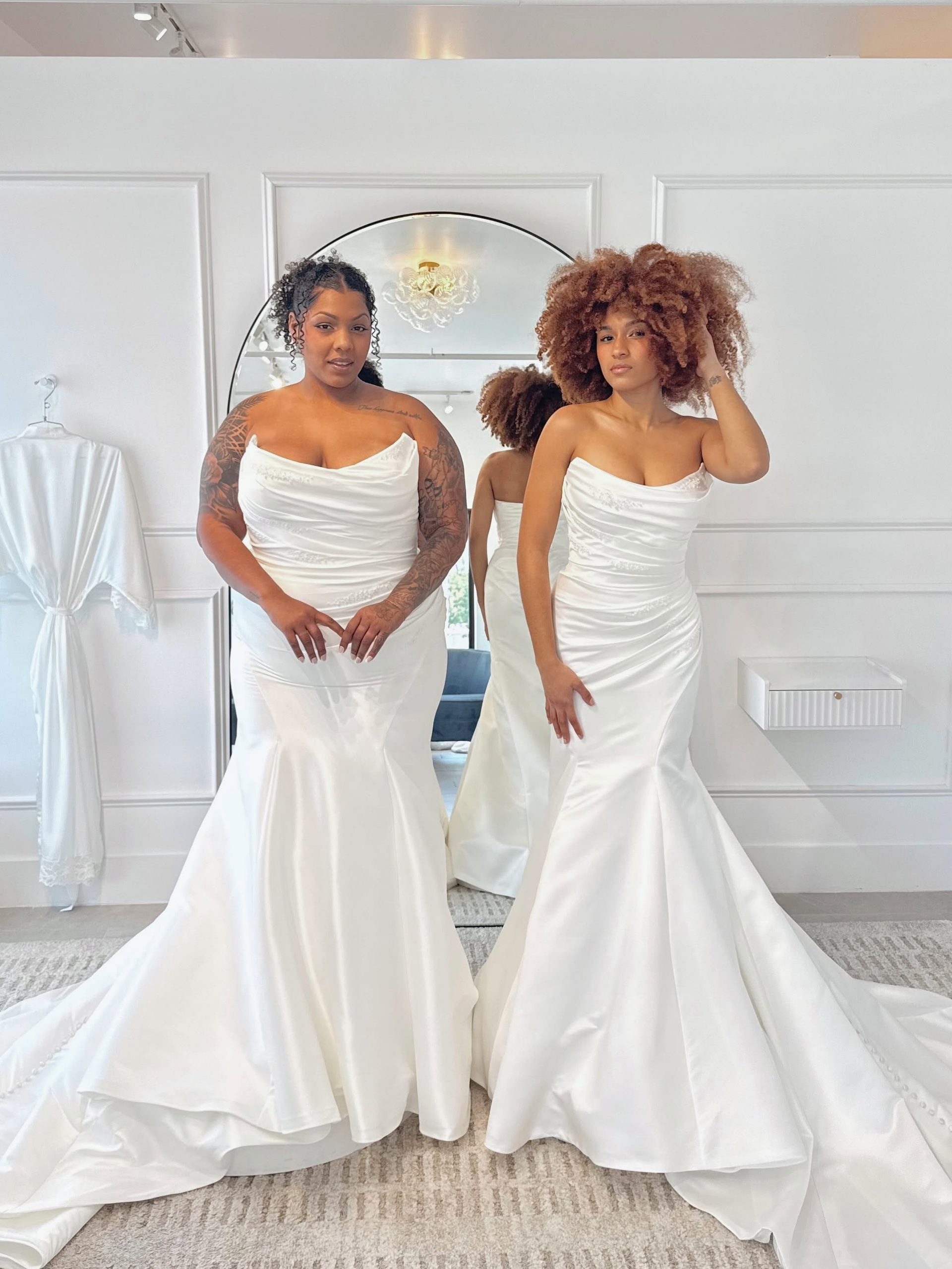 Two brides wearing elegant satin mermaid wedding dresses with strapless necklines at Savvy Bridal.