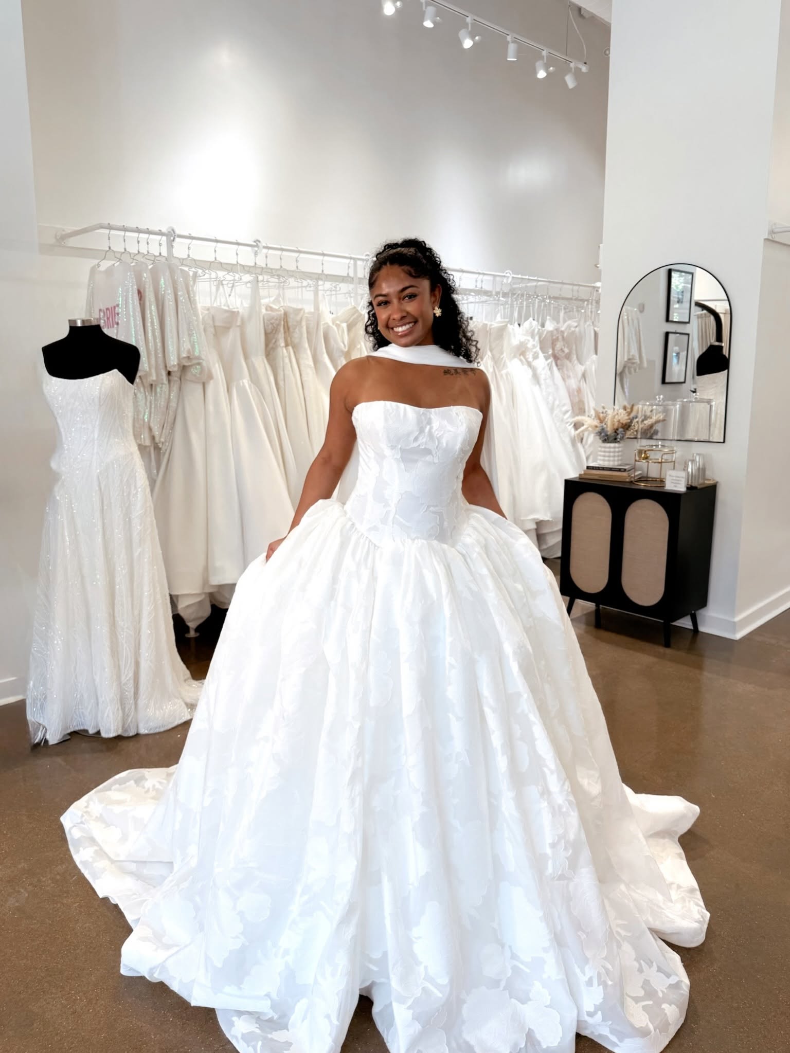 Smiling bride modeling a strapless floral ball gown with a full skirt at Savvy Bridal.