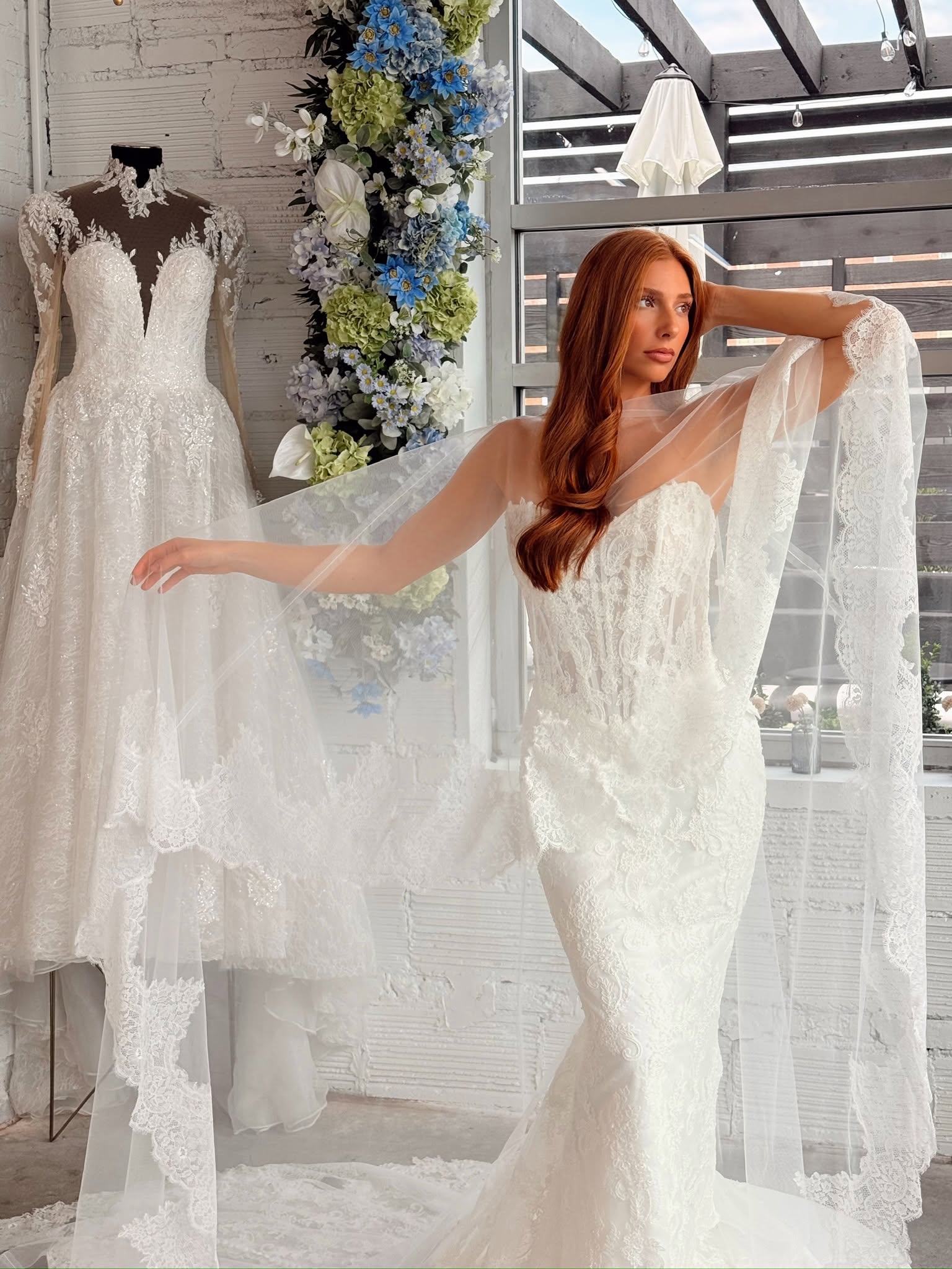 Model wearing a fitted lace wedding dress with a sheer lace-trimmed veil at Savvy Bridal.