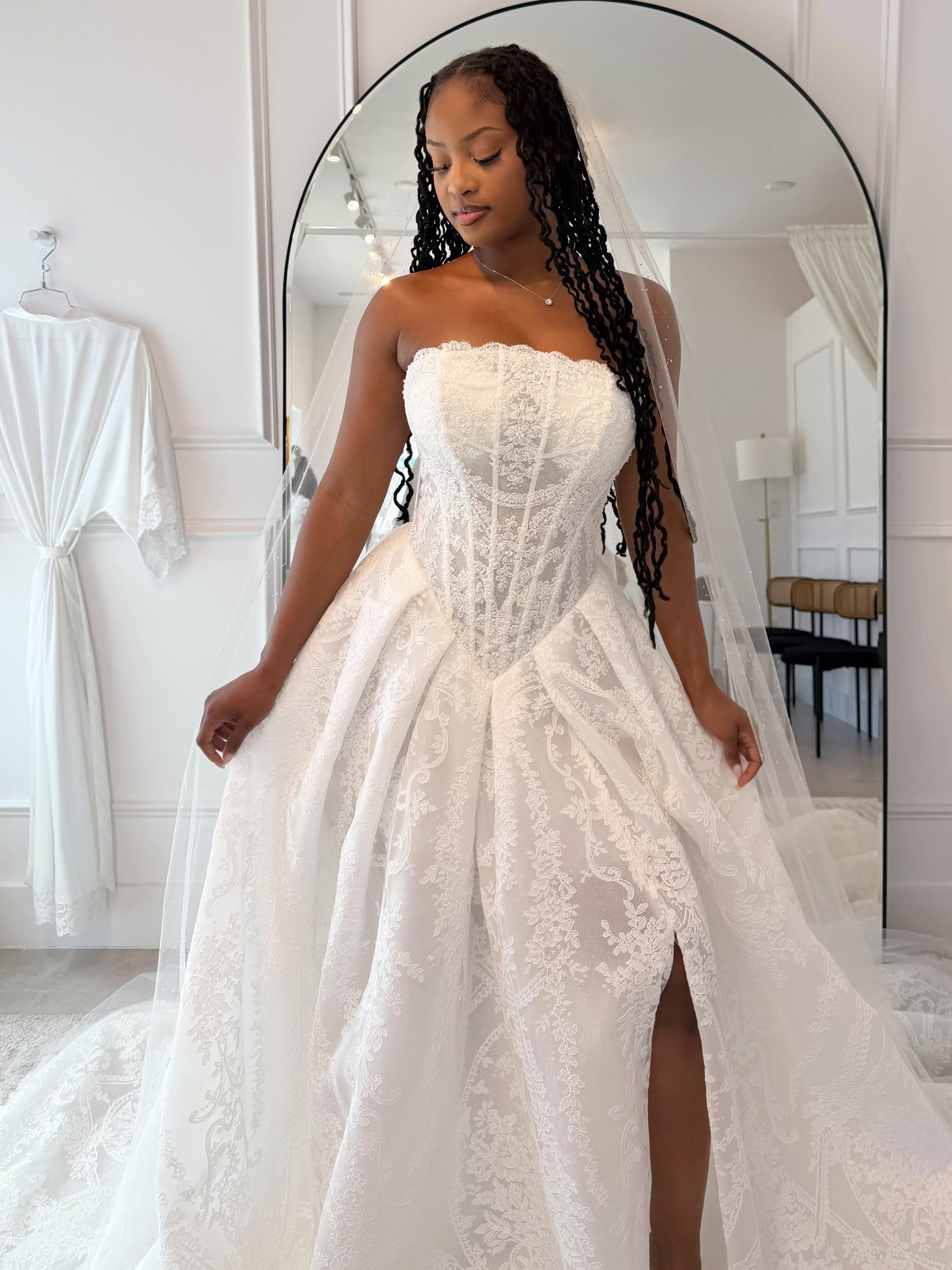 Bride modeling a strapless lace ball gown with a corset bodice, thigh-high slit, and delicate veil.