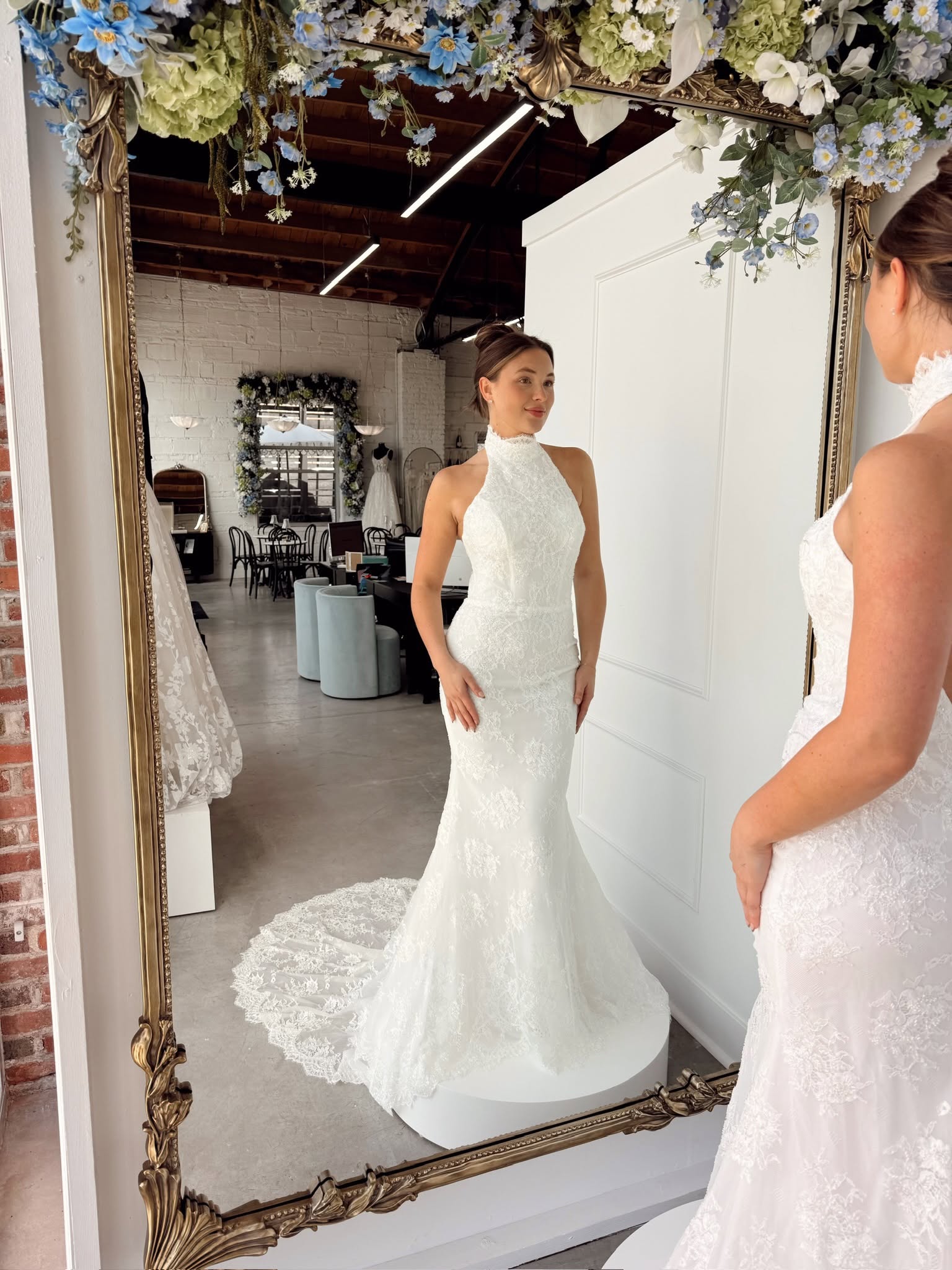 Bride admiring a fitted high-neck lace wedding dress with a flowing train in an ornate mirror.