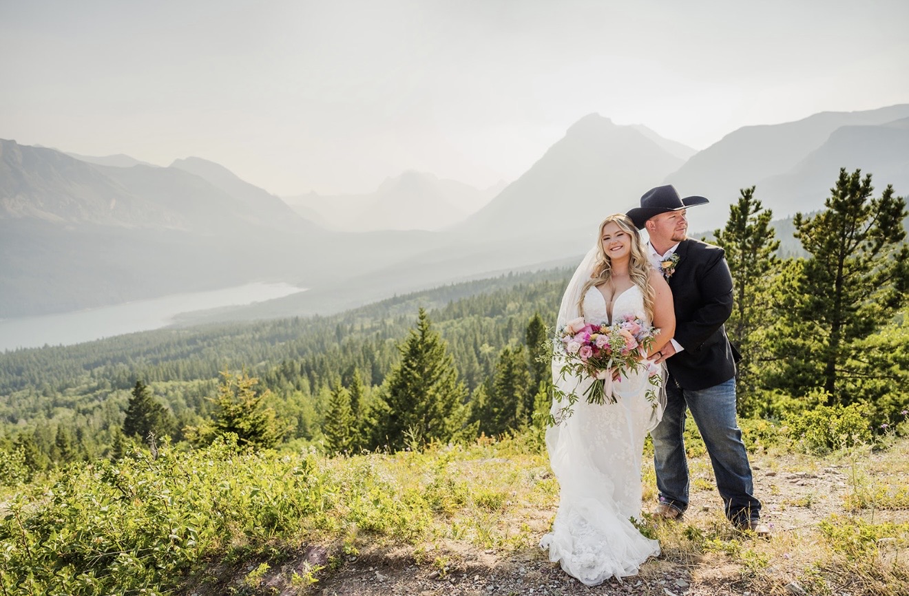 Savvy Bride Annabelle and Zack posing in their wedding attire overlooking the mountains and lake at Glacier National Park.