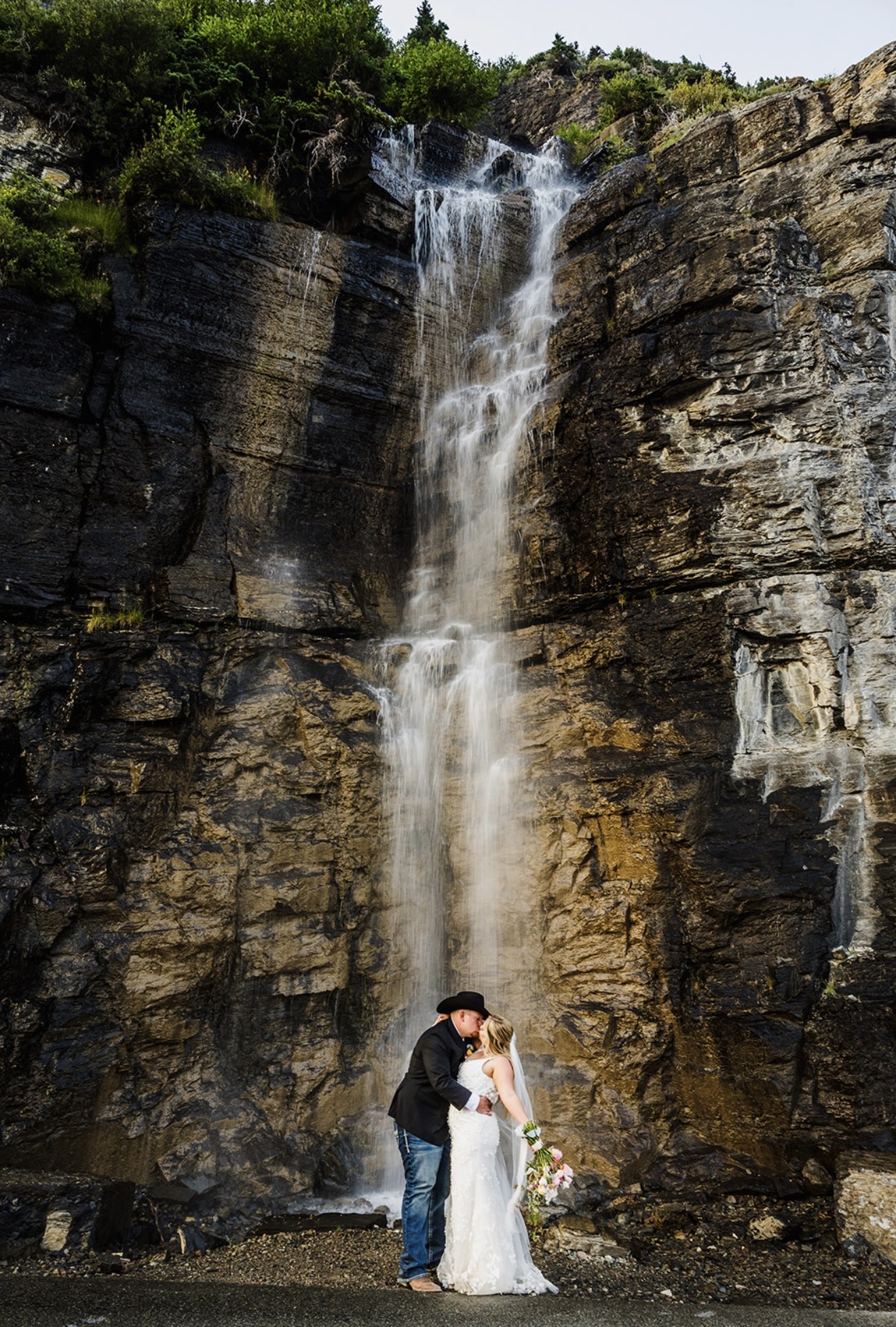 Annabelle and Zack sharing a romantic kiss beneath a towering waterfall during their Glacier National Park wedding.