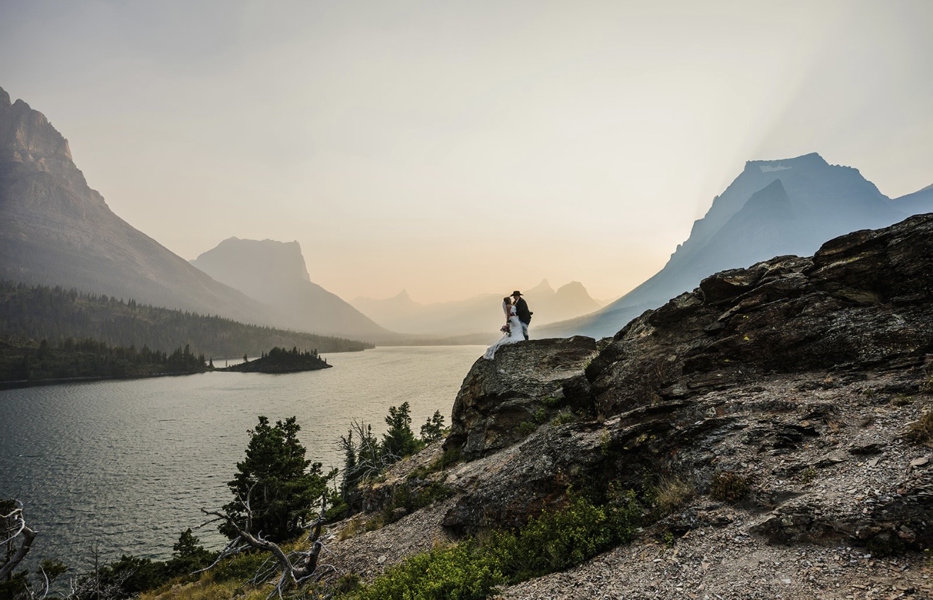 Savvy Bride Annabelle and Zack posing in their wedding attire overlooking the mountains and lake at Glacier National Park.