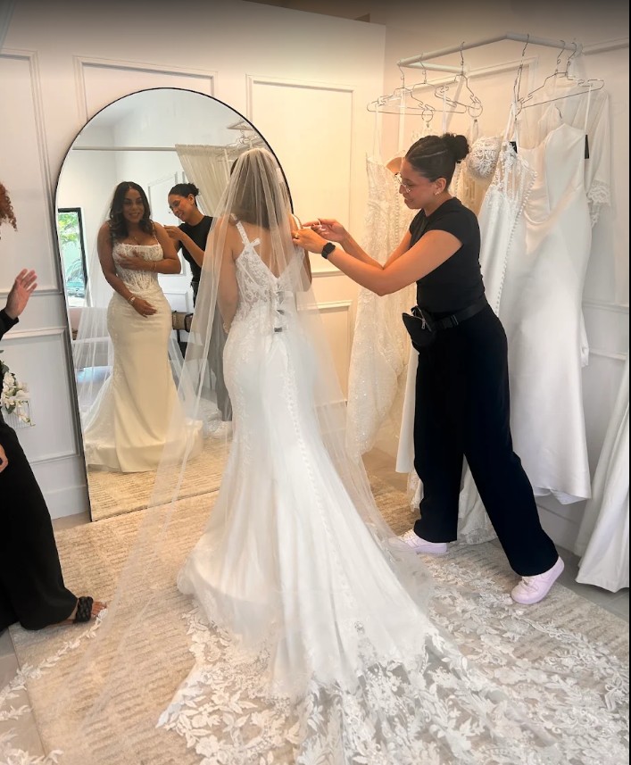 Savvy Bridal stylist adjusts a bride’s veil as she admires her dream wedding dress in the mirror.