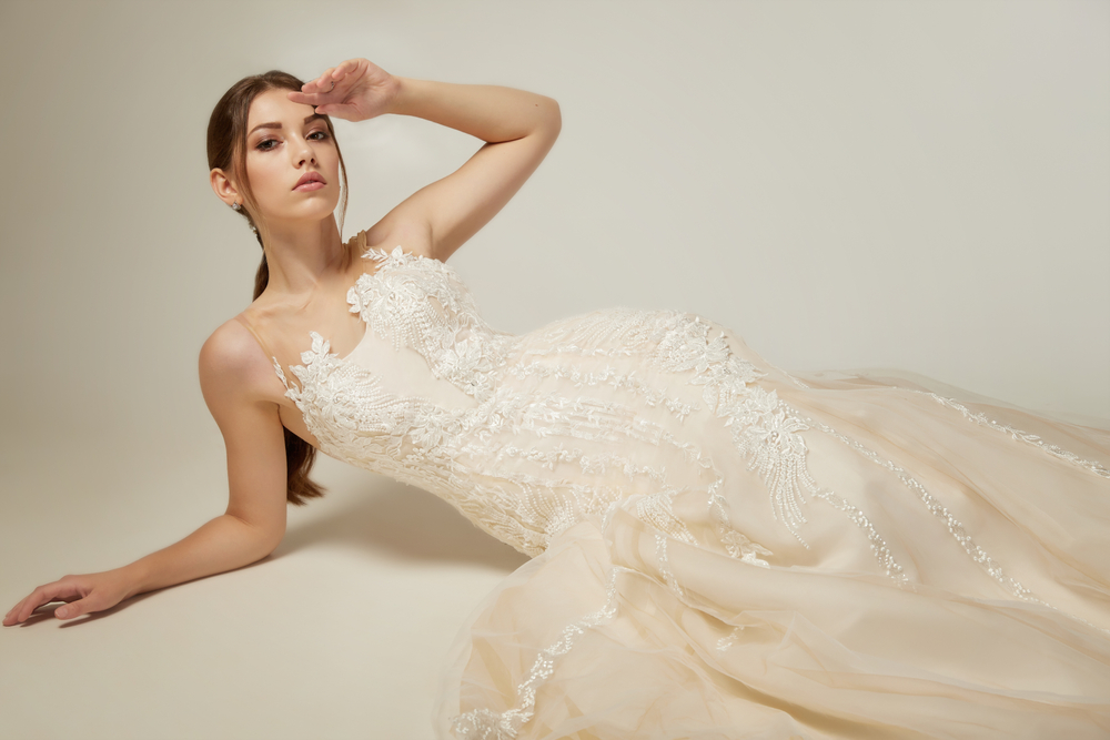 Bride in lace detail wedding gown lounging on a white background